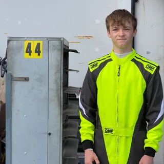 Jonah in his neon yellow and black race suit beside a pit rack with a yellow number 44 sign