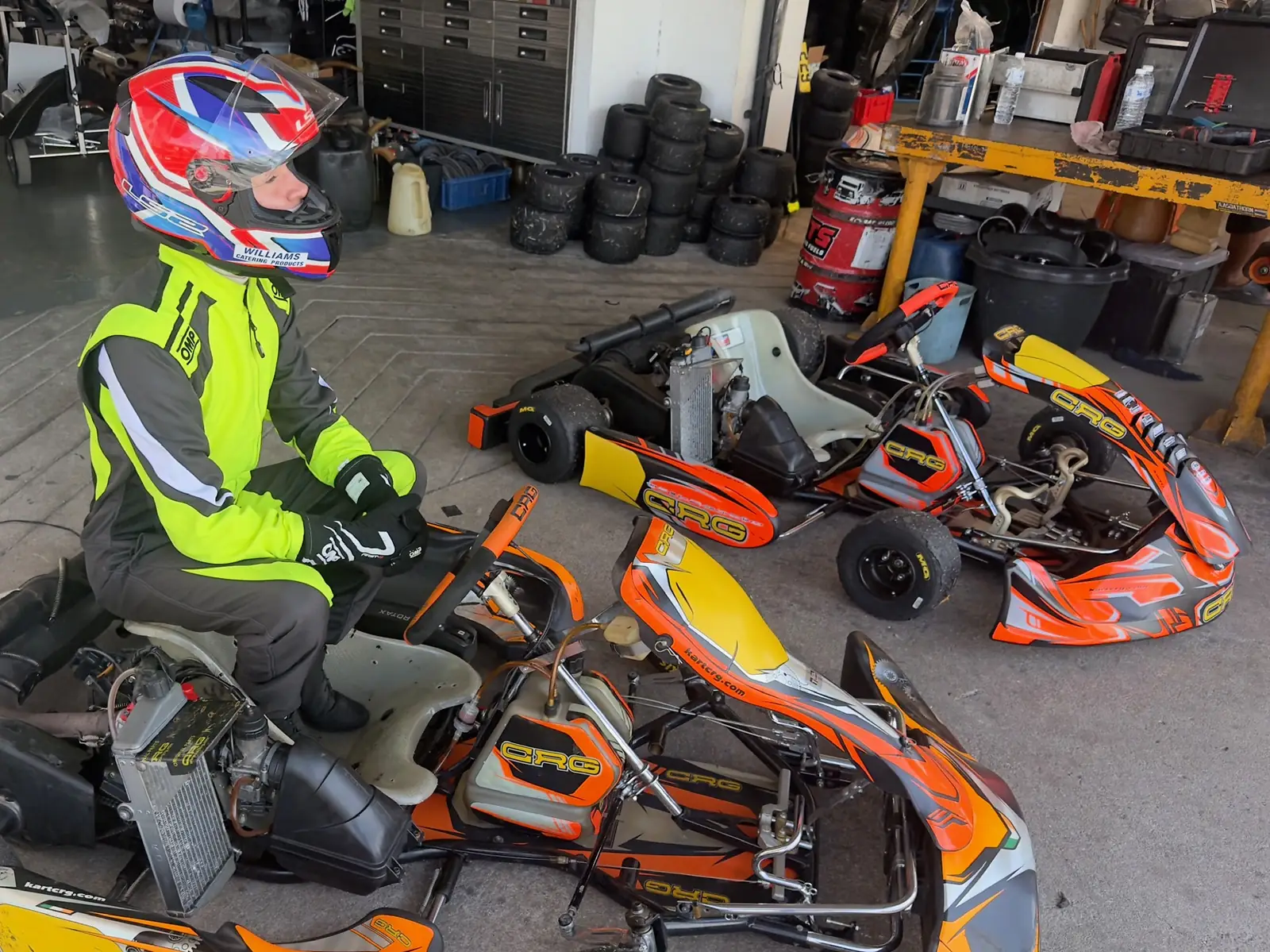 Jonah in his helmet on a test day in Thailand, beside an orange kart in the garage
